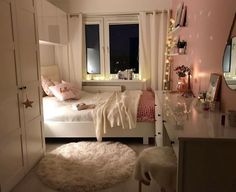 a bedroom with pink walls, white furniture and lights on the window sills