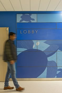 a man walking past a lobby sign in front of a blue wall with the words lobby on it