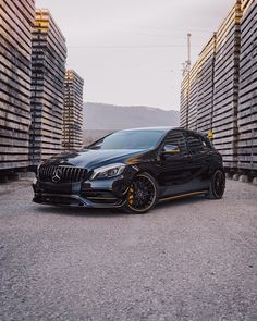 a black mercedes cla parked in front of stacks of wooden pallets on the side of a road