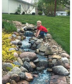 a young boy is playing in the water by some rocks and grass with his feet up