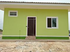 a green and white house sitting on top of a dirt field