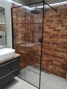 a bathroom with a brick wall and glass shower stall, sink and mirror on the side