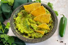 guacamole with tortilla chips in a bowl next to green peppers