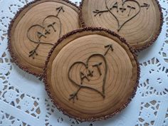 three wooden slices with carved hearts and arrows in the center on a lace doily