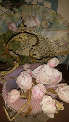 some pink roses are sitting on a table next to an antique fan and other decorative items