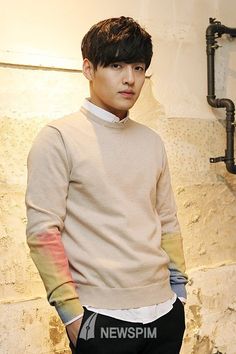 a young man standing in front of a brick wall wearing a sweater and black pants