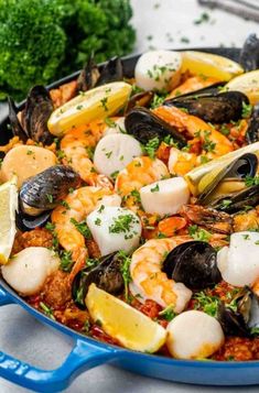 a skillet filled with seafood and clams on top of a table next to lemon wedges