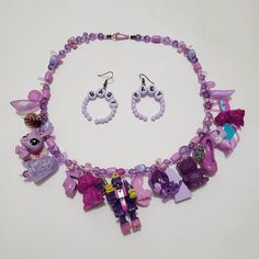 This is a purple themed charm necklace that I crafted out of vintage toys and charms. It is full of exciting variety and textures. Comes with matching earrings. Playful Purple Dangle Jewelry, Handmade Pink Themed Jewelry, Handmade Themed Pink Jewelry, Unique Purple Dangle Necklaces, Fun Purple Dangle Jewelry, Purple Jewelry With Dangling Charms For Gifts, Whimsical Purple Necklace For Gifts, Whimsical Purple Necklace For Gift, Purple Dangle Charms Jewelry