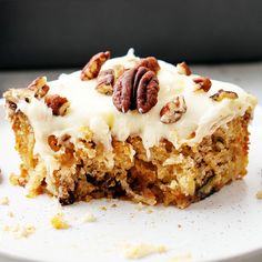 a piece of carrot cake with white frosting and pecans on top, sitting on a plate