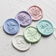 four wax seals with flowers on them sitting in front of a white wall and sand