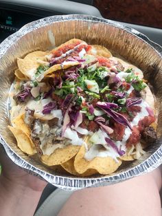 a person holding up a metal bowl filled with nachos and coleslaw