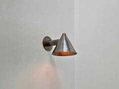 a wall light mounted on the side of a white wall with a cone shaped shade