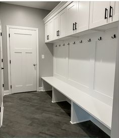 a white bench sitting in the middle of a room next to a wall mounted coat rack