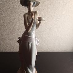 a statue of a woman holding a cup and saucer in her hands, with a hat on top of her head