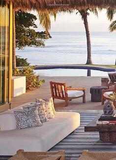 a living room with couches and chairs near the water in front of a palm tree