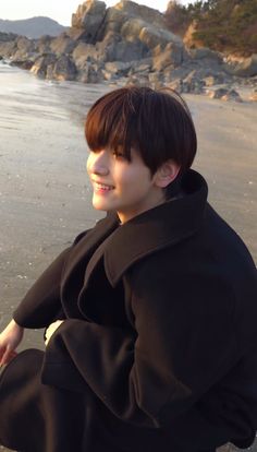 a young man sitting on the beach smiling