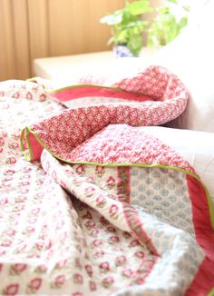 a bed covered in a pink and white quilt next to a potted green plant