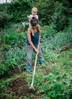 a woman holding a child while digging in the grass