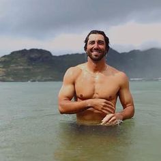 a shirtless man standing in the water with his hands together and smiling at the camera