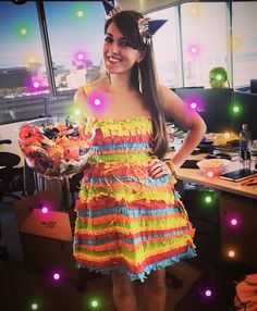 a woman standing in an office wearing a colorful dress and holding a bowl of flowers