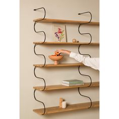 a woman standing in front of a wall shelf holding a bowl with an orange on it