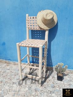 a wooden chair with a straw hat on it next to a cactus and a blue wall