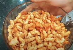 a person holding a glass bowl filled with macaroni and cheese