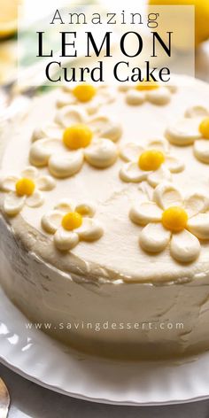 a lemon cake with white frosting and yellow flowers on top, sitting on a plate