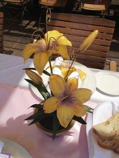 yellow flowers in a vase sitting on a table with bread and wine glasses next to it