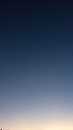 two people standing on the beach looking out at the ocean and one person is flying a kite