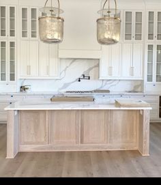 a large kitchen with white cabinets and marble counter tops, two hanging lights over the island