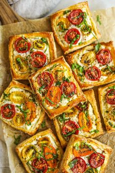 several square pieces of bread with tomatoes and cheese on them sitting on a piece of parchment paper