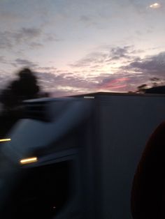 a blurry photo of a truck driving down the road at dusk with trees in the background