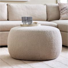 a white ottoman sitting on top of a wooden floor next to a couch and coffee table