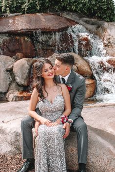 a bride and groom sitting on a rock in front of a waterfall at their wedding