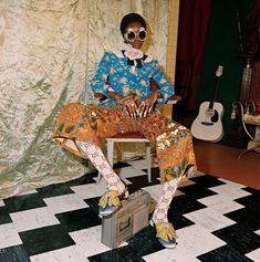 a woman sitting on top of a suitcase in front of a wall covered with curtains