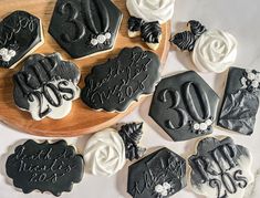 decorated cookies with black and white frosting on a wooden platter next to flowers