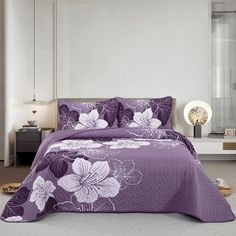 a bed with purple flowers on it in a white and gray room, next to a night stand