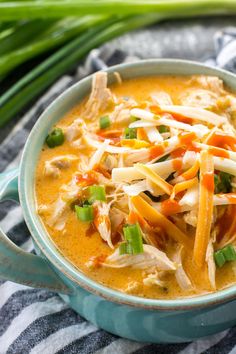 a blue bowl filled with chicken and cheese soup on top of a striped towel next to green onions