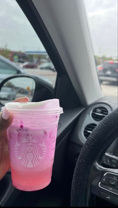 a hand holding a cup with pink liquid in it next to a car steering wheel