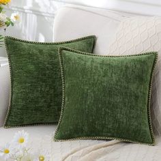 two green pillows sitting on top of a white couch next to flowers and vases