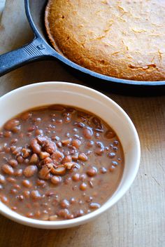 baked beans in a bowl next to a skillet with bread on the counter top