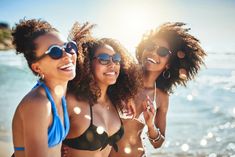 three beautiful women in bikinis standing on the beach with sun shining through their sunglasses