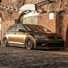 a gold vw golf r parked in front of an old brick building on a cobblestone street