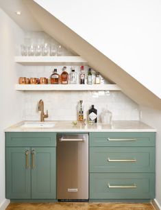 a kitchen with green cabinets and white counter tops under a slanted ceiling above the sink is a stainless steel dishwasher