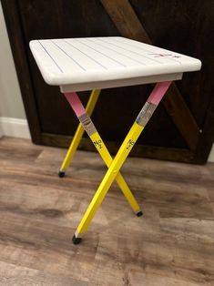 a white and yellow folding stool with writing on the seat is in front of a wooden door