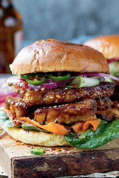 a chicken sandwich with lettuce, onions and carrots on a cutting board