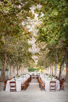 an outdoor dining area with tables, chairs and chandelier hanging from the trees