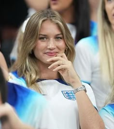 a beautiful blonde woman sitting in the stands with her hand on her chin and looking at the camera