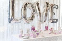 a table topped with lots of silver balloons and love letters on top of each other